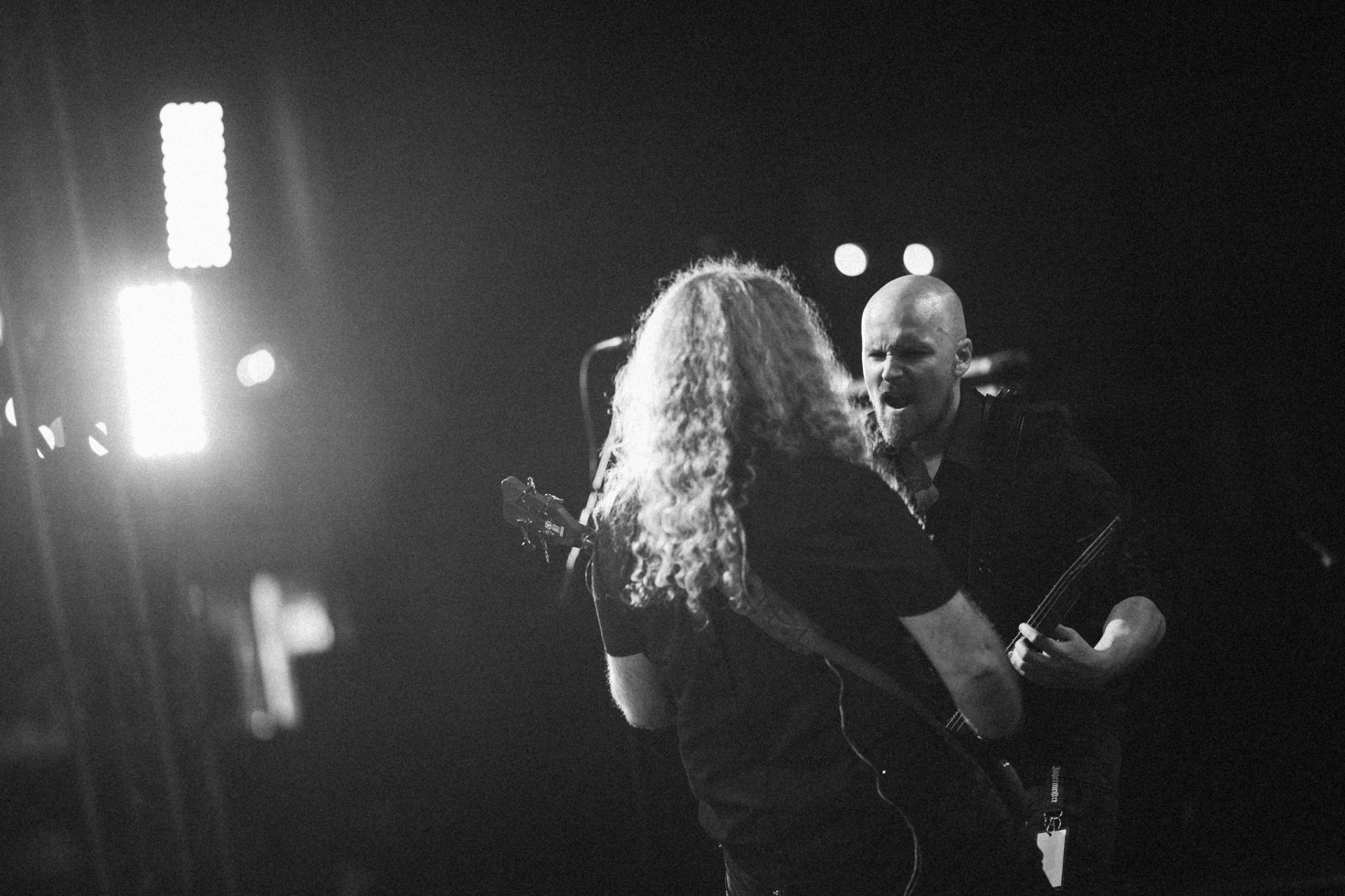 Black-and-white concert photo, singer and guitarist performing in strong light, with fog and lights in the background.